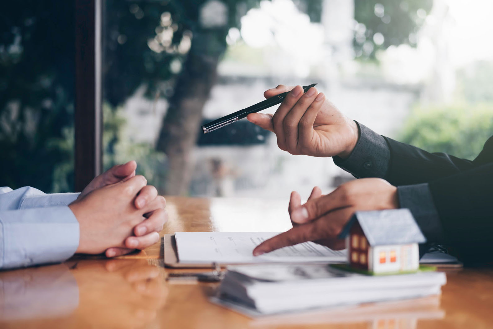 two people talking over a desk with a house paper weight on top of papers